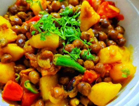 A bowl of Chola Bhuna (spicy chickpeas) garnished with fresh coriander, served with naan and lemon wedges – a perfect Bangladeshi iftar dish.